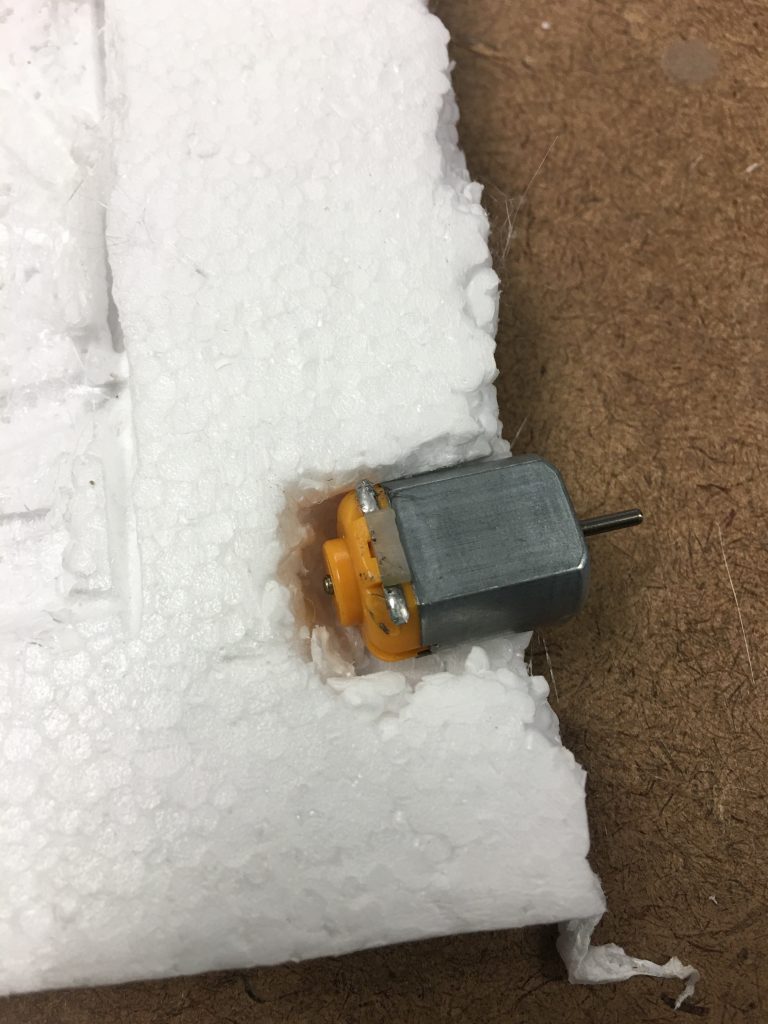 A dc motor with no wires is in a crevice in a block of white foam.