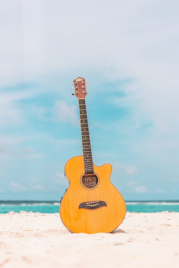 brown acoustic guitar on white sand during daytime