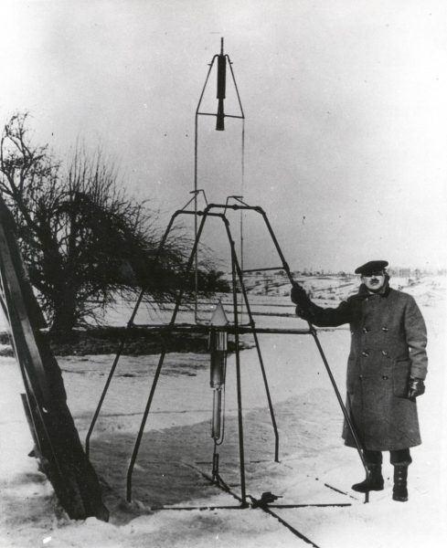 Robert Goddard, bundled against the cold New England weather of March 16, 1926, holds the launching frame of his most notable invention â€” the first liquid-fueled rocket. (CC0 1.0)
