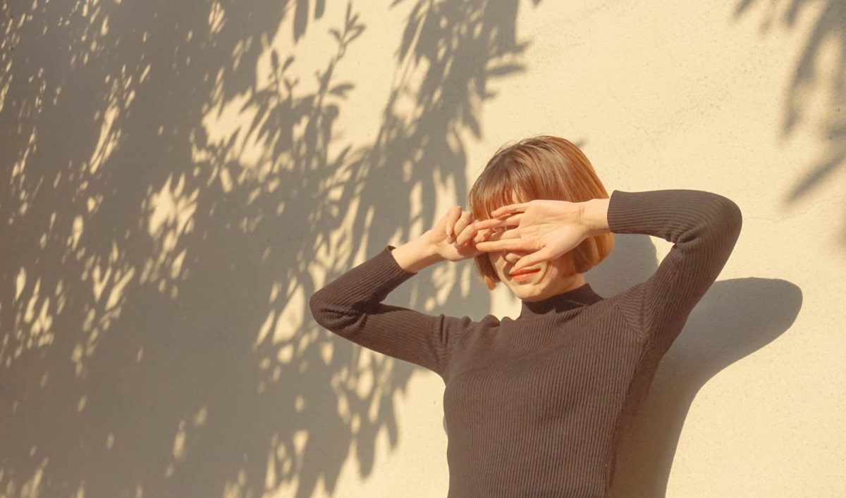 A stylish woman covers her eyes from the sun, enjoying a bright outdoor day.