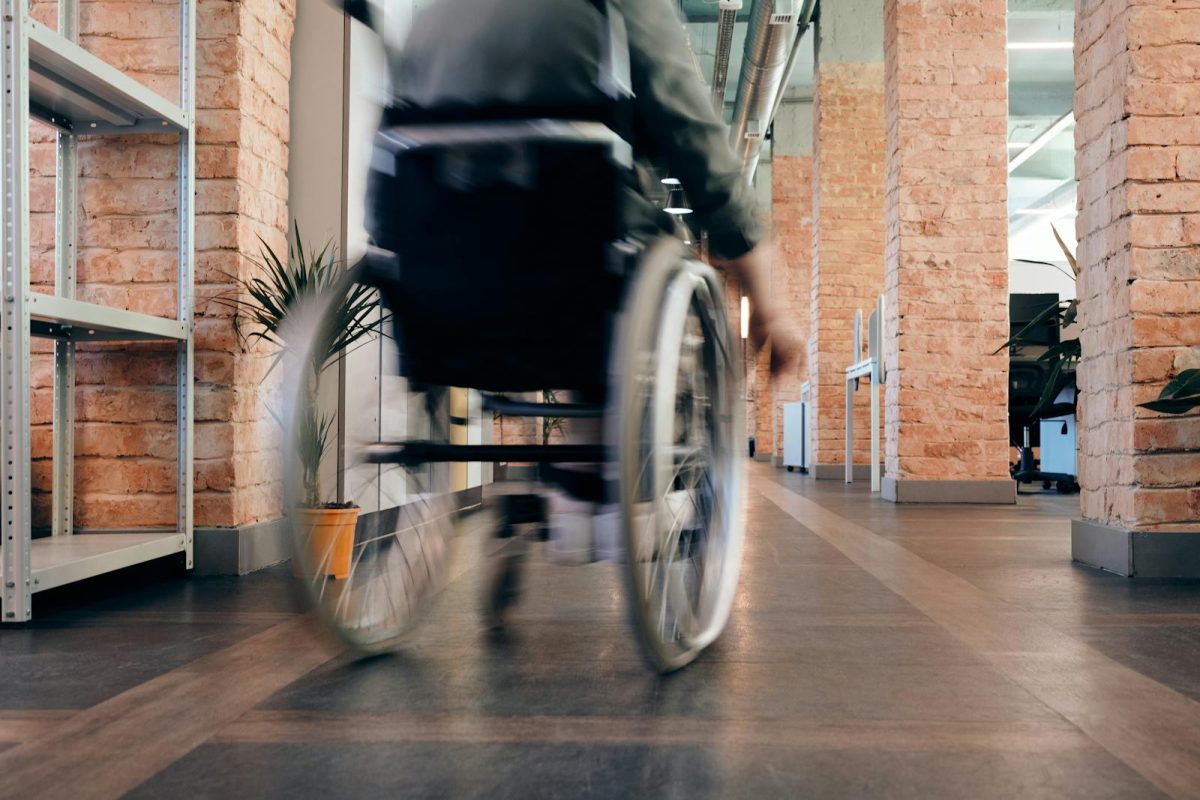 Blurred motion of a person in a wheelchair moving quickly through an indoor office hallway.