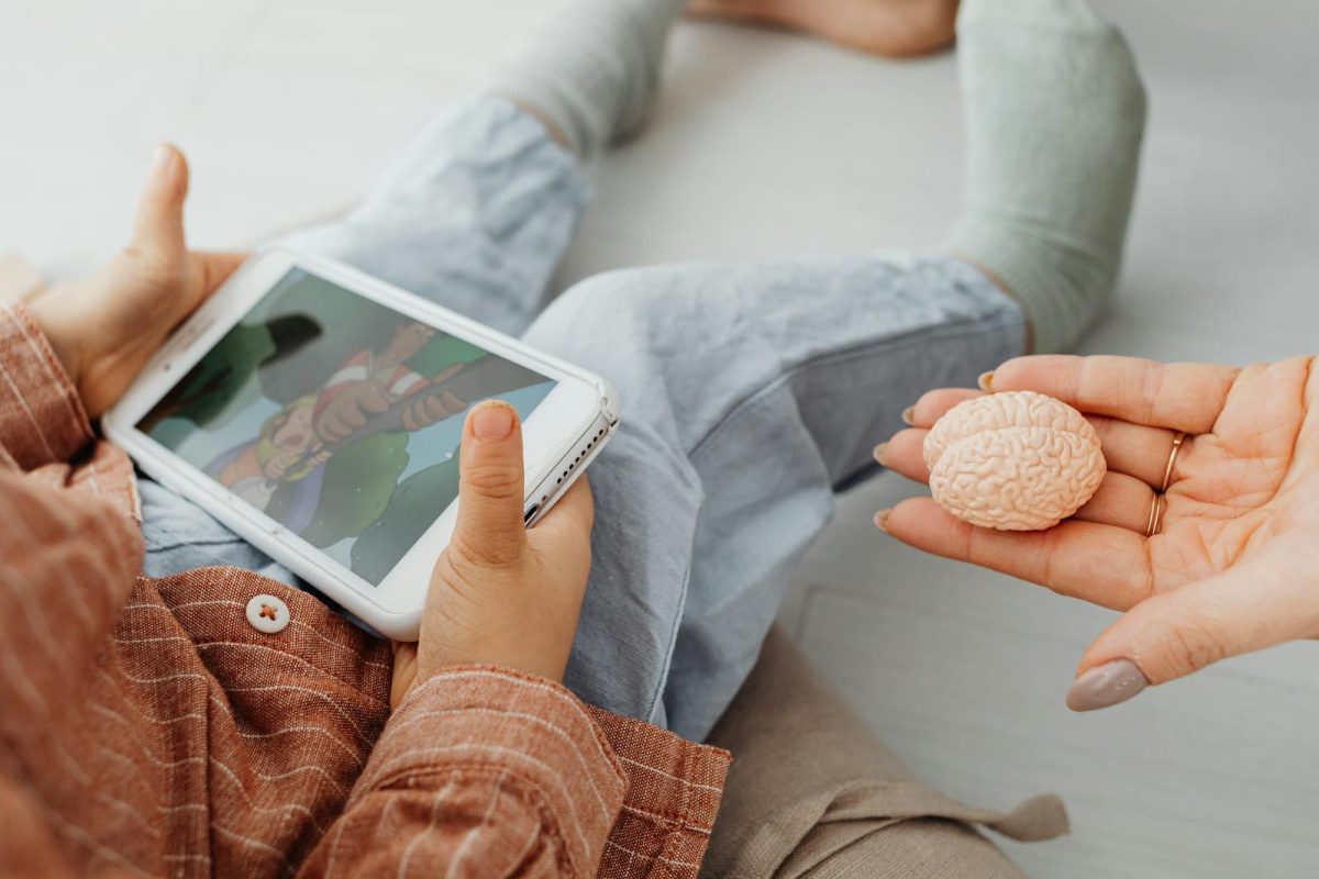 A child watches a cartoon on a tablet as an adult holds a brain model.